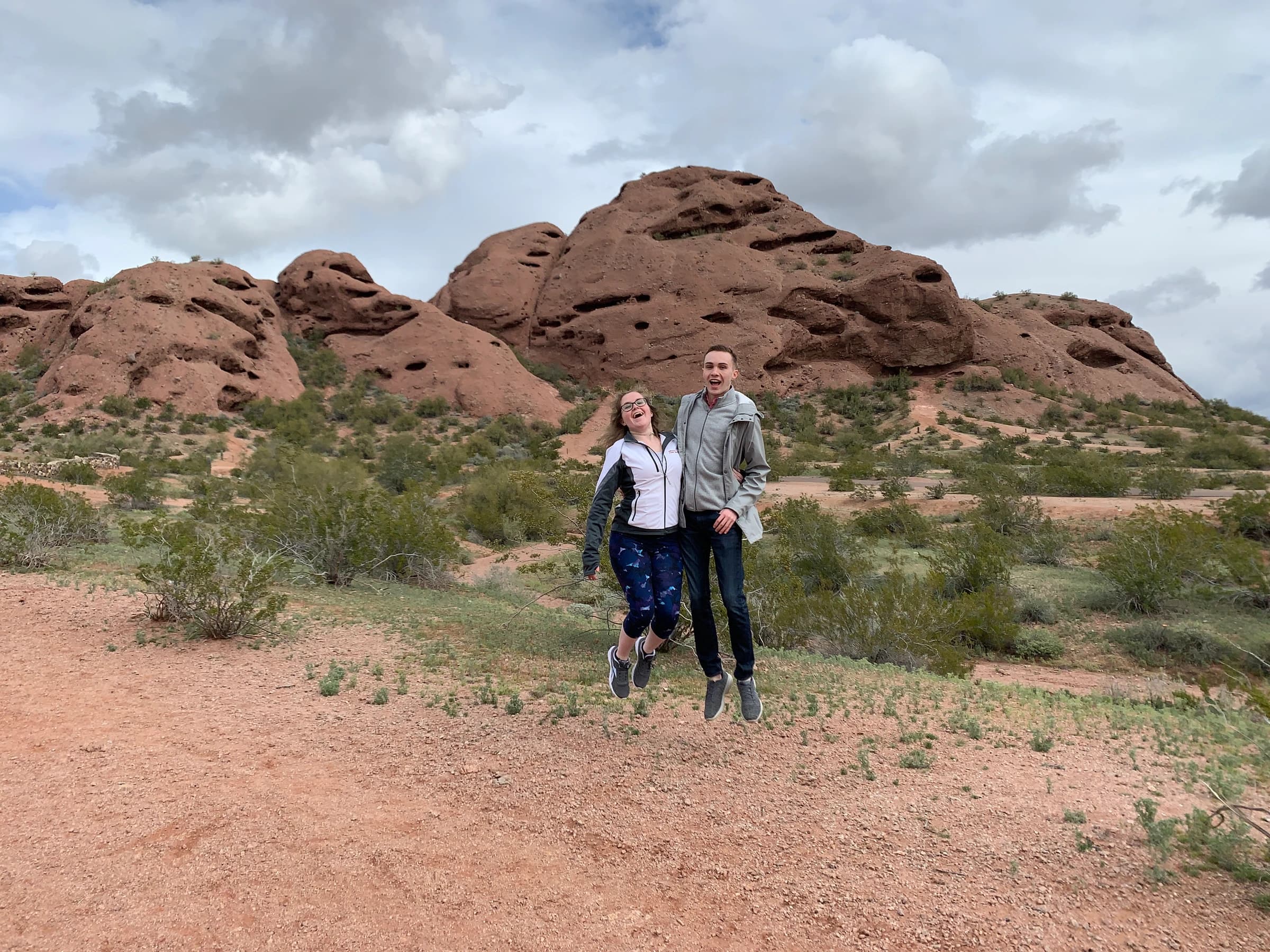 Rachel and Reid jumping in the air in front of red desert rock formations in Arizona